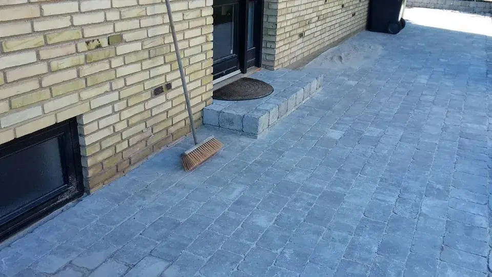 Terrasse med fliser langs et gult murstenshus